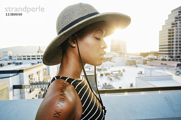 Nachdenkliche schwarze Frau mit Sonnenhut auf dem Dach