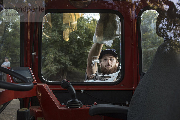 Kaukasischer Mann wäscht Fenster eines Traktors