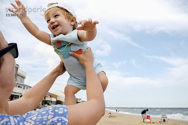 Kaukasische Mutter hebt ihren kleinen Sohn am Strand hoch