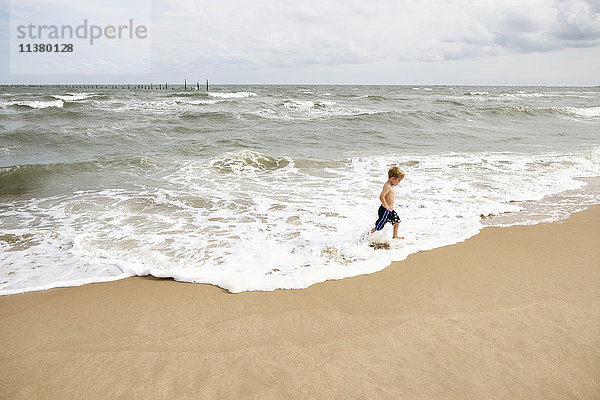 Kaukasischer Junge läuft in den Wellen am Strand