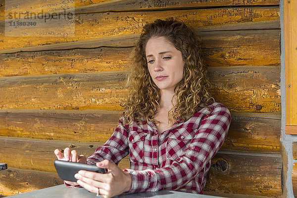 Kaukasische Frau lehnt an einer Holzwand und schreibt eine SMS auf ihrem Handy