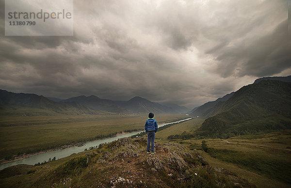 Kaukasischer Junge in der Nähe eines Flusses in einer bewölkten Landschaft stehend