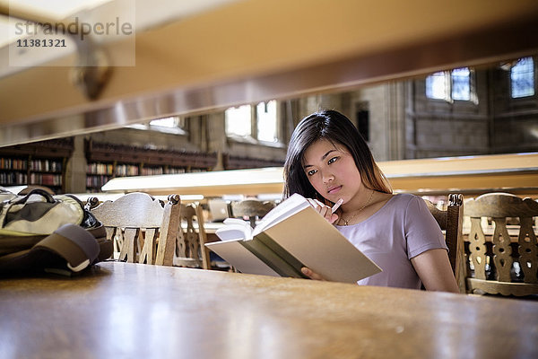 Chinesische Frau sitzt in der Bibliothek und liest ein Buch