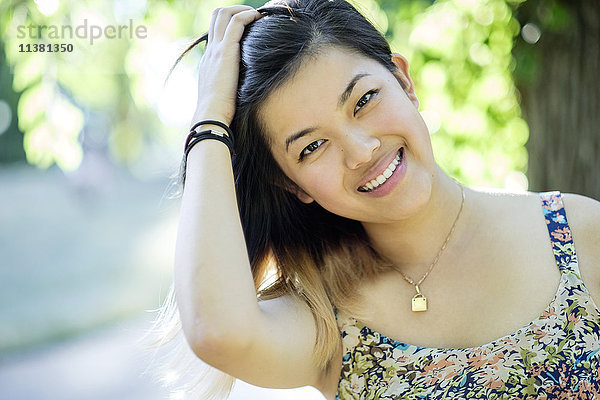 Porträt einer lächelnden Chinesin mit Hand im Haar