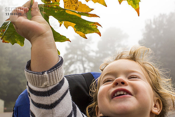 Lächelndes kaukasisches Mädchen hält Herbstblatt