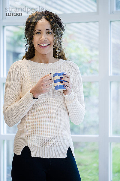 Frau steht am Fenster und hält eine Kaffeetasse