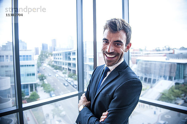 Porträt eines lächelnden hispanischen Geschäftsmannes  der in der Nähe eines Fensters posiert