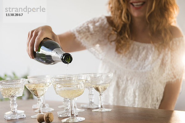 Lächelnde kaukasische Frau gießt Champagner in Coupés ein