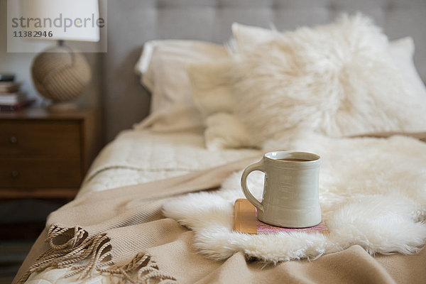 Kaffeetasse und Buch auf Fell auf dem Bett