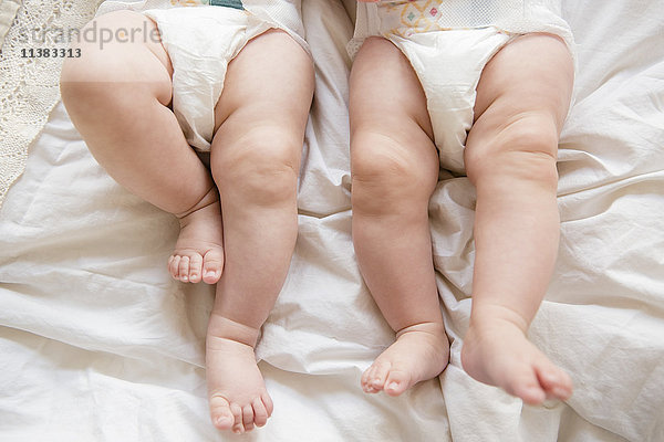 Beine von kaukasischen Zwillingsmädchen auf dem Bett liegend