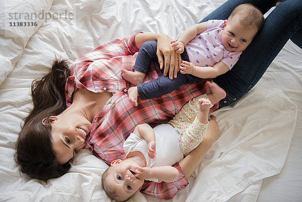 Kaukasische Mutter auf dem Bett liegend mit Zwillingstöchtern