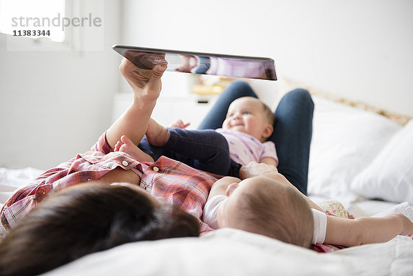 Kaukasische Mutter auf dem Bett mit Zwillingsbaby Töchter mit digitalen Tablette