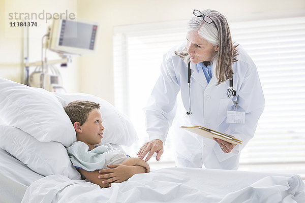 Kaukasischer Arzt im Gespräch mit einem Jungen im Krankenhausbett