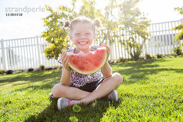 Kaukasisches Mädchen sitzt im Gras und isst Wassermelone