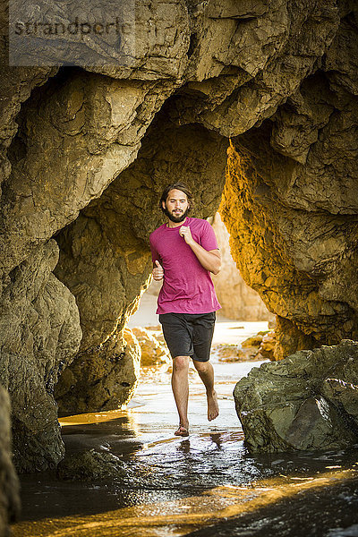 Kaukasischer Mann  der unter einer Felsformation am Strand läuft