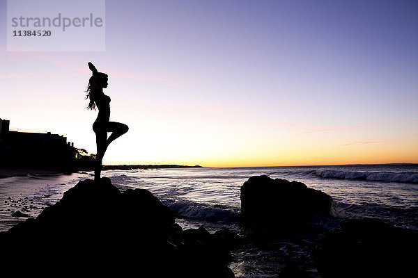 Silhouette einer kaukasischen Frau  die auf einem Felsen am Strand balanciert