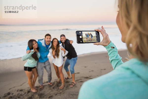 Frau fotografiert Freunde am Strand mit Mobiltelefon