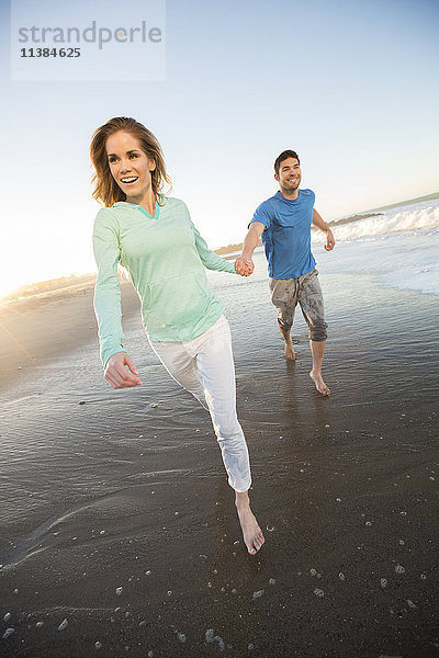 Paar hält sich an den Händen und läuft am Strand