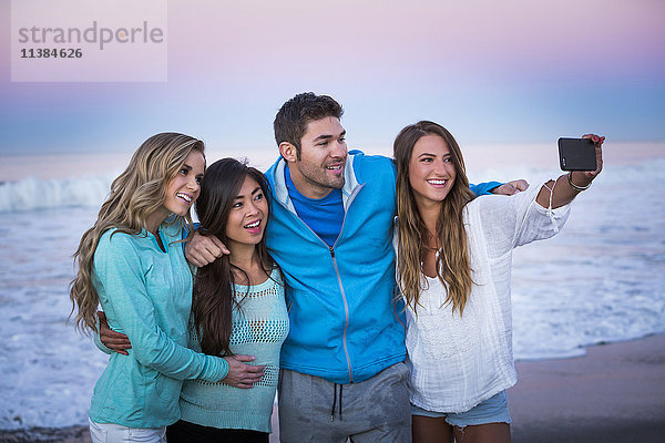 Freunde posieren für Handy-Selfie am Strand bei Sonnenuntergang