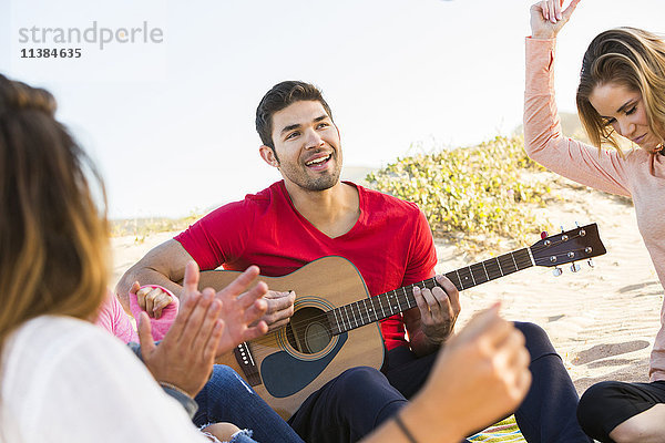 Mann spielt Gitarre für Freunde am Strand