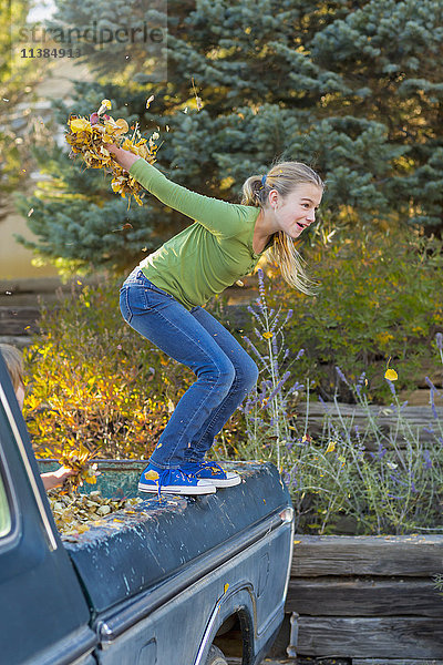 Kaukasisches Mädchen hält Herbstblätter und springt von einem Lastwagen