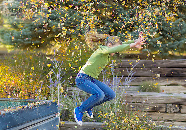 Kaukasisches Mädchen  das Herbstblätter wirft und von einem Lastwagen springt