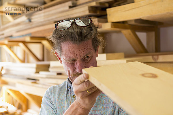 Kaukasischer Tischler  der in der Werkstatt ein Holzbrett beäugt
