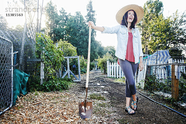 Lachende kaukasische Frau  die sich im Garten auf eine Schaufel stützt