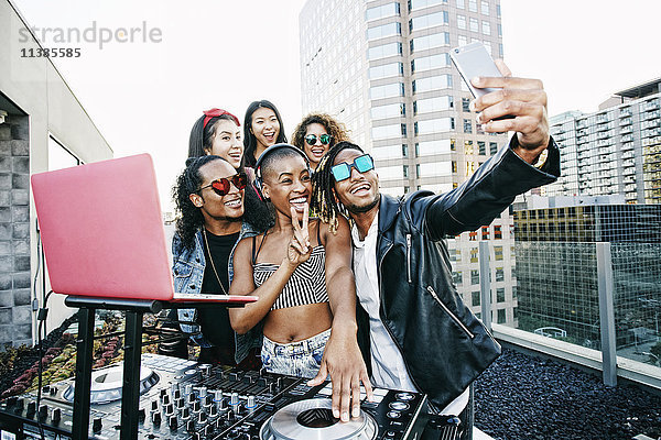 Freunde posieren für ein Handy-Selfie mit einem DJ auf einem Hausdach