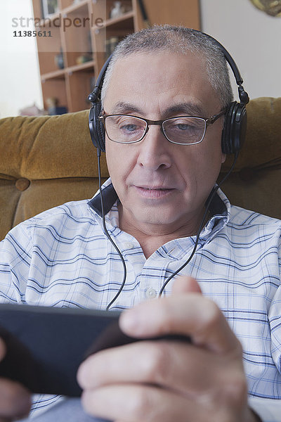 Neugieriger hispanischer Mann  der mit Kopfhörern sein Handy abhört
