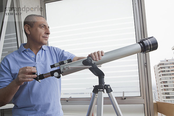 Hispanischer Mann hält Teleskop am Fenster