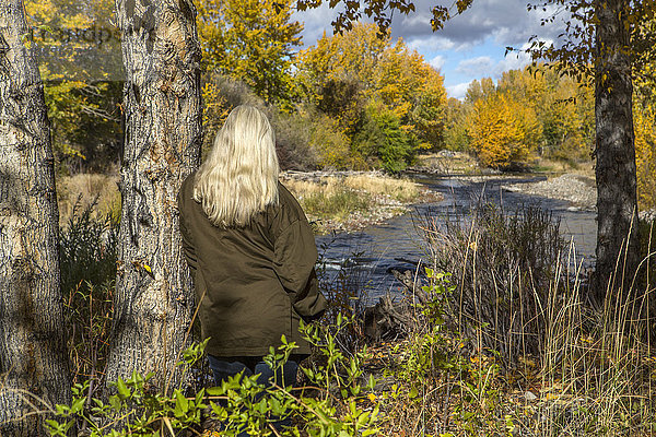 Kaukasische Frau lehnt an einem Baum in der Nähe eines Flusses