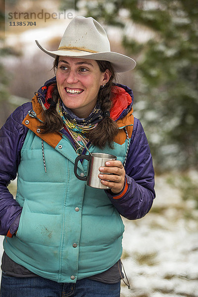 Lächelnde kaukasische Frau hält Metallbecher im Winter
