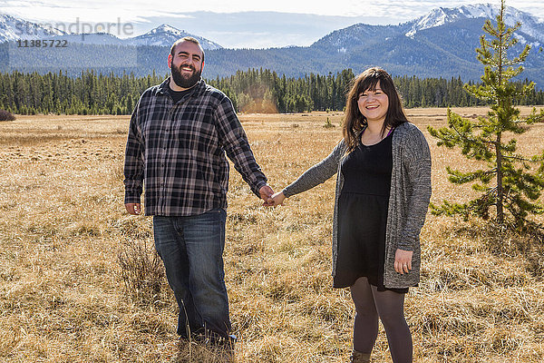 Lächelndes kaukasisches Paar hält sich auf einem Feld die Hände