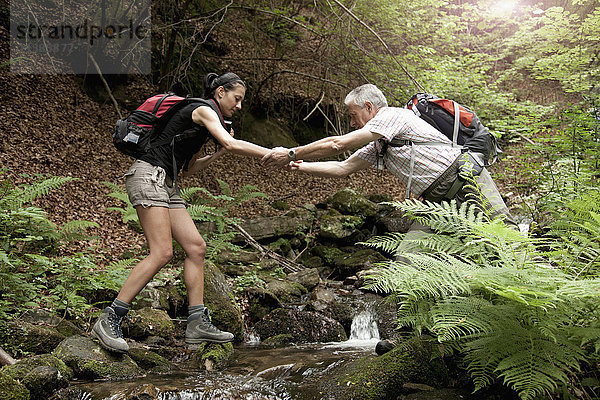 Kaukasischer Mann hilft Frau beim Überqueren eines Waldflusses