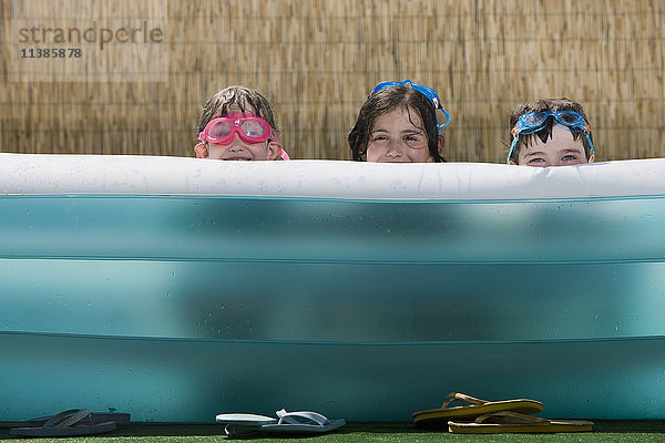 Lächelnde kaukasische Kinder  die sich in einem aufblasbaren Schwimmbecken verstecken