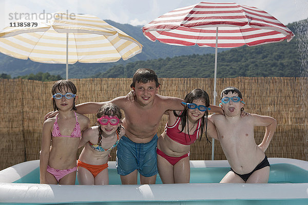 Lächelnde kaukasische Kinder posieren im aufblasbaren Schwimmbecken