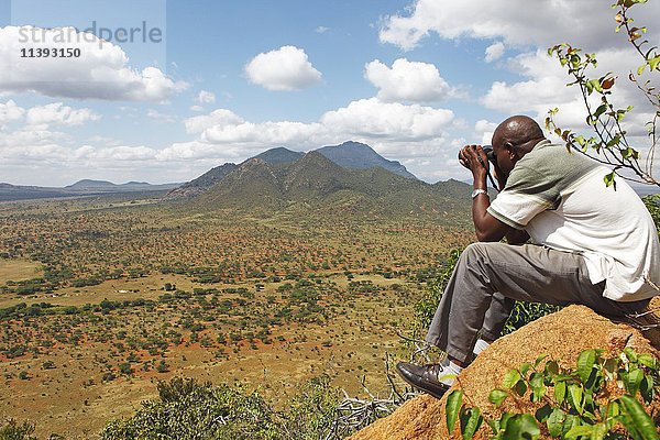 Mann mit Fernglas mit Blick auf die Ngulia Hills und das Rhino Valley  Tsavo West National Park  Taita-Taveta County  Kenia  Afrika