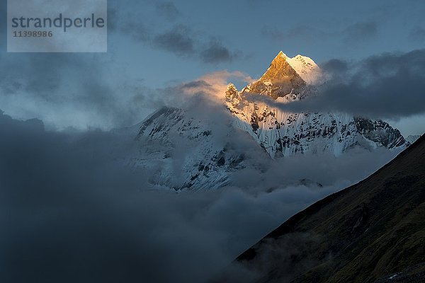 Blick auf den Gipfel des Berges Machapuchare bei Sonnenuntergang  teilweise von Monsunwolken verdeckt  Chomrong  Kaski District  Nepal  Asien