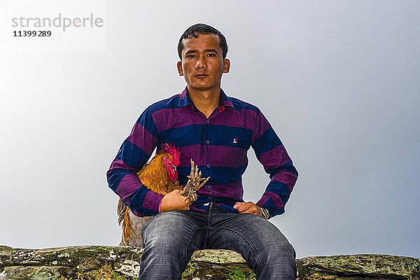 Einheimischer Mann sitzt mit einem Hahn  der bald im Khadga Devi Mandir Tempel geopfert werden soll  Darsain Hindu Festival  Bandipur  Tanahun  Nepall