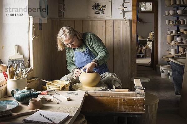 Keramikwerkstatt  Frau bearbeitet Ton mit Rippe auf Töpferscheibe  im Hintergrund Trockengestell  Pittenhart  Oberbayern  Deutschland  Europa