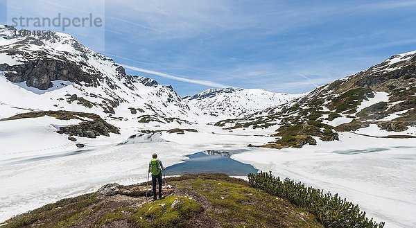 Junger Mann  Wanderer mit Blick auf zugefrorenen See  Unterer Giglachsee  Berglandschaft mit Schneeresten  Rohrmoos-Obertal  Schladminger Tauern  Schladming  Steiermark  Österreich  Europa