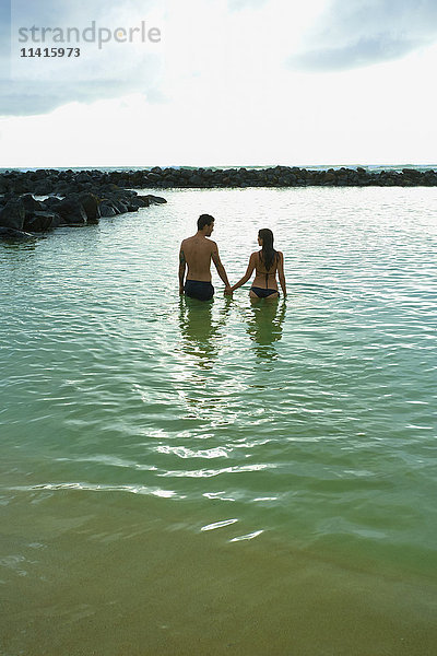 Ein Paar hält sich an den Händen und geht in den Ozean vor Lydgate Beach; Kauai  Hawaii  Vereinigte Staaten von Amerika'.