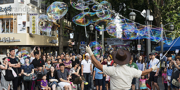 Zuschauer beobachten einen Straßenkünstler  der mit langen Stäben Seifenblasenkunst macht; Seoul  Südkorea'.
