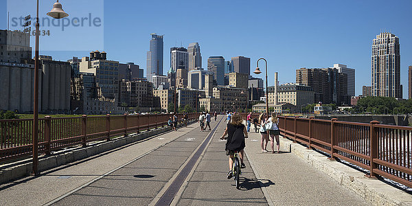 Radfahrer und Fußgänger auf einer Brücke mit Blick auf die Skyline von Minneapolis; Minneapolis  Minnesota  Vereinigte Staaten von Amerika'.