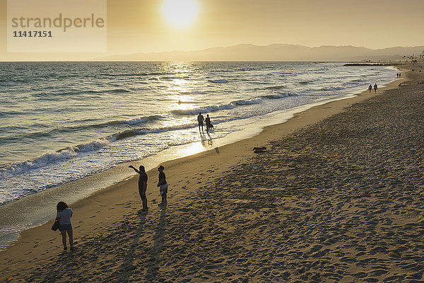 Menschen spazieren am Venice Beach bei Sonnenuntergang; Venice Beach  Kalifornien  Vereinigte Staaten von Amerika'.