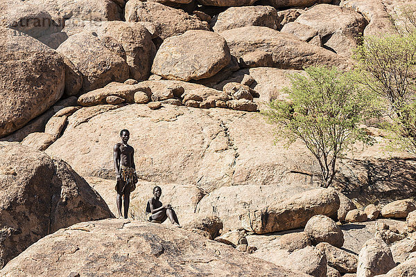 Junge Männer in traditioneller Kleidung des Damara-Volkes posieren im Lebenden Museum der Damara vor einem felsigen Hintergrund; Namibia'.