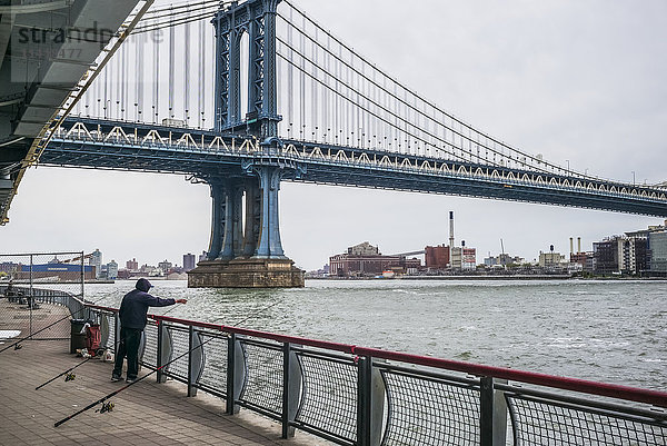 Manhattan-Brücke und ein Mann  der an der Reling steht und im East River angelt; New York City  New York  Vereinigte Staaten von Amerika