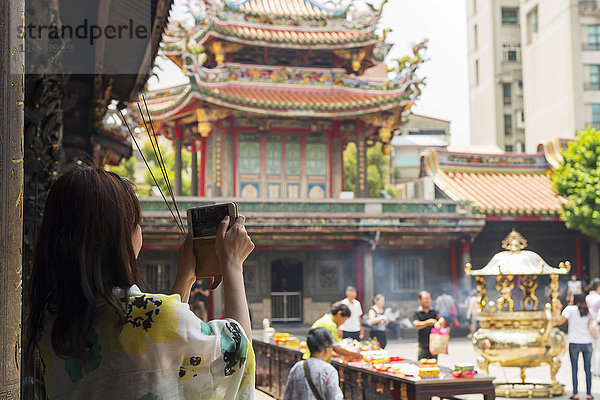 Buddhistischer Longshan-Tempel im Stadtzentrum von Taipeh  Menschen beten und verbrennen Weihrauch  während ein Tourist ein Foto macht; Taipeh  Taiwan  China'.