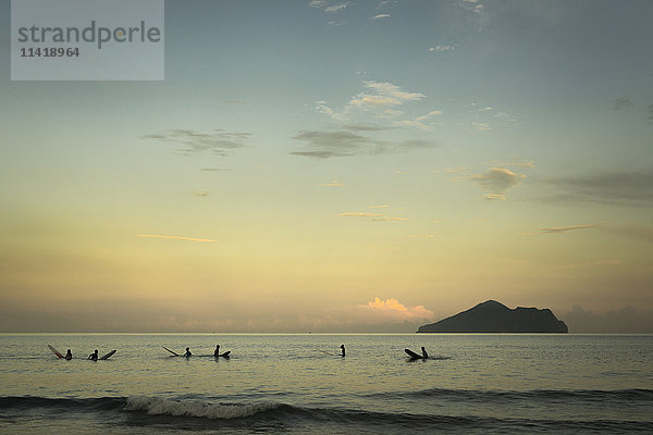 Surfer  die auf die Wellen warten  mit der Schildkröteninsel im Hintergrund bei Sonnenuntergang  Strand Waiao  Bezirk Yilan  Taiwan  China